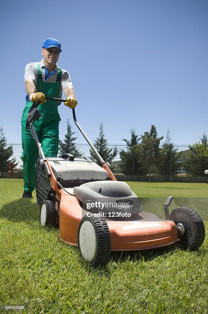 Male Gardener in Overalls Pushing Lawn Mower