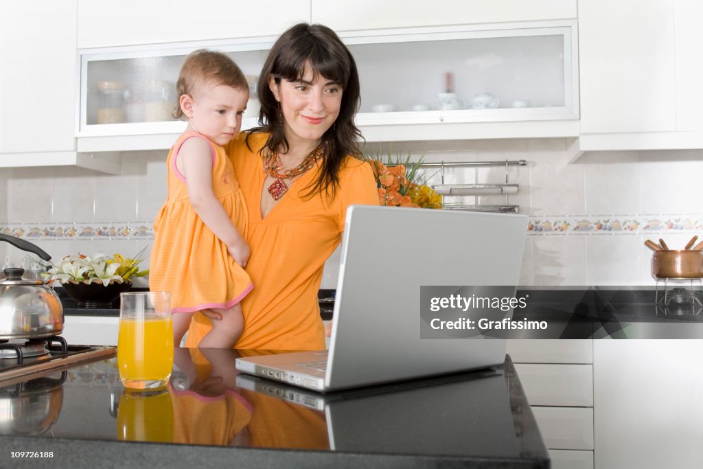 Baby with mother and laptop in the kitchen