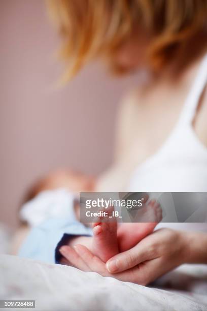 donna in fase di allattamento al seno del neonato e delicatamente tenendo il piede del bambino - ambientazione tranquilla foto e immagini stock