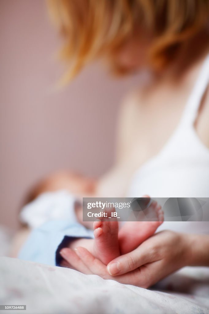 Woman nursing a tiny newborn baby and holding his feet