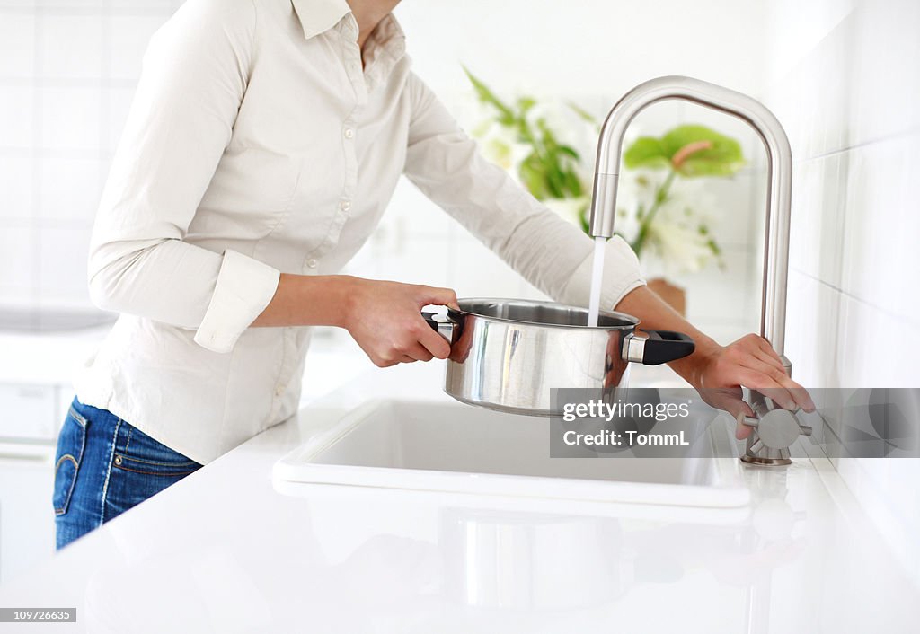 The woman is at the sink with a saucepan.