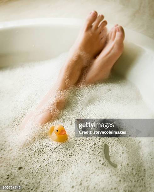 female's legs in bubblebath with yellow rubber ducky - badeend stockfoto's en -beelden