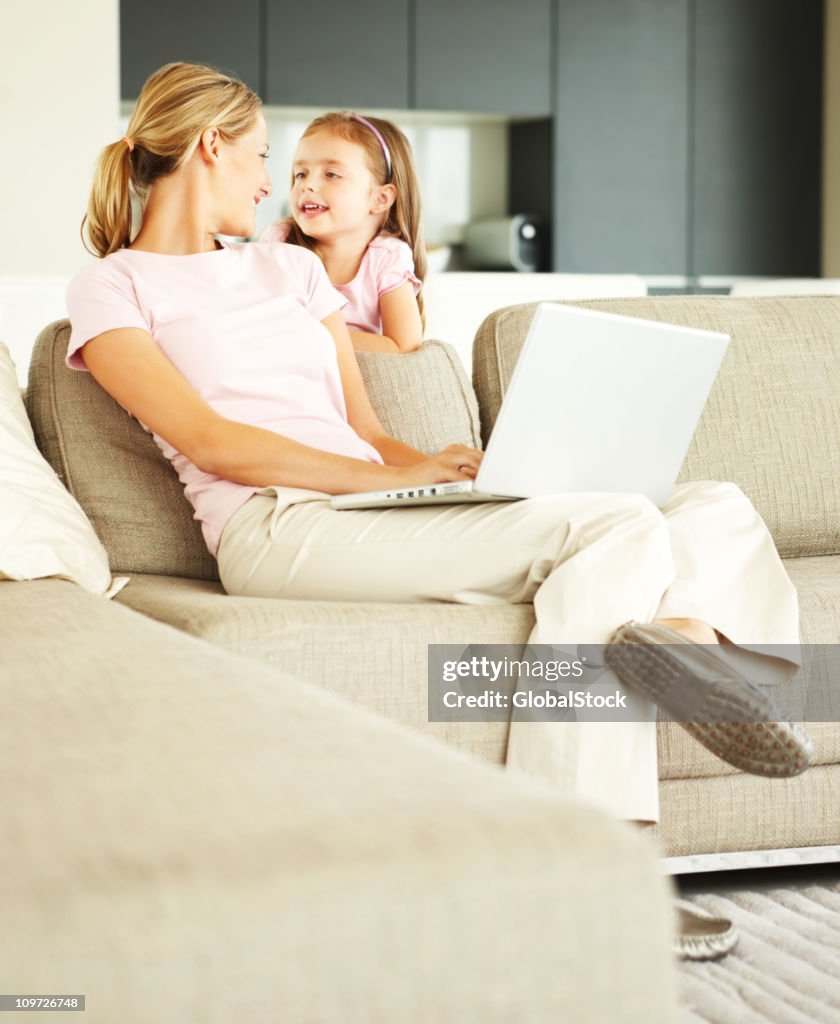 Giovane donna lavorando sul portatile con la figlia in piedi accanto al suo