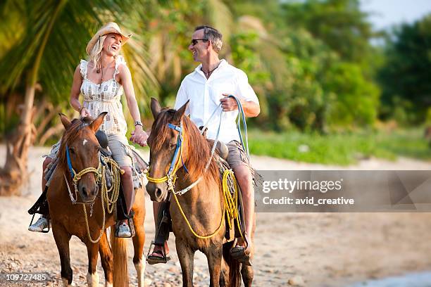 vacation lifestyles-couple riding horses on beach at sunset - horse riding stockfoto's en -beelden