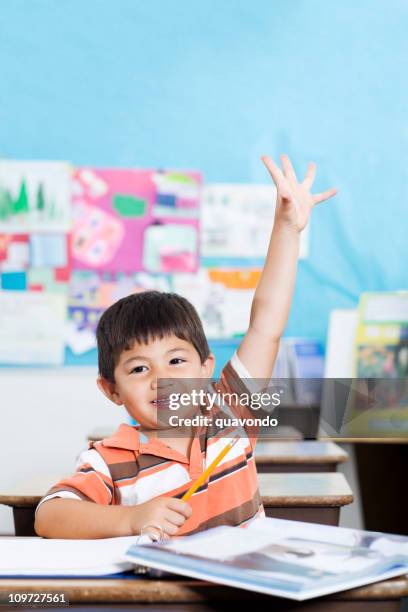 adorable little boy raising hand in elementary classroom - boy asking stock pictures, royalty-free photos & images