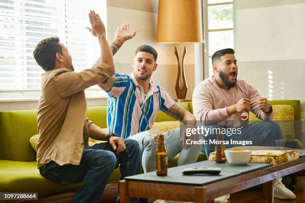 male fans are enjoying soccer match at home - celebrating in sofa stock pictures, royalty-free photos & images