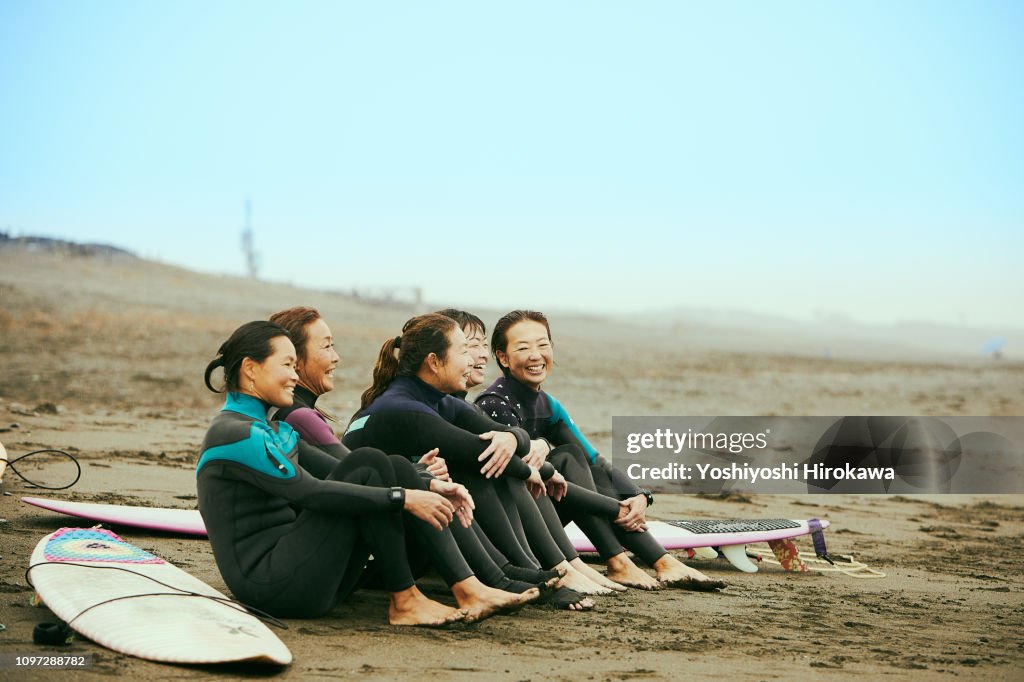 Surfer women are talking on beach in the rain