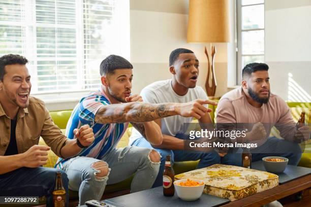 excited friends watching match on tv at home - watching stock pictures, royalty-free photos & images