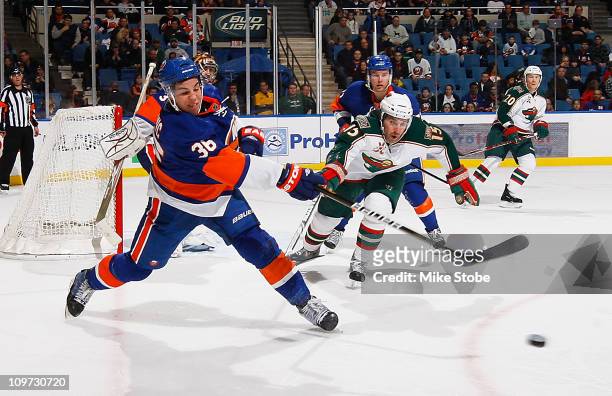 Travis Hamonic of the New York Islanders clears the puck as he's being pursued by Andrew Brunette of the Minnesota Wild on March 2, 2011 at Nassau...