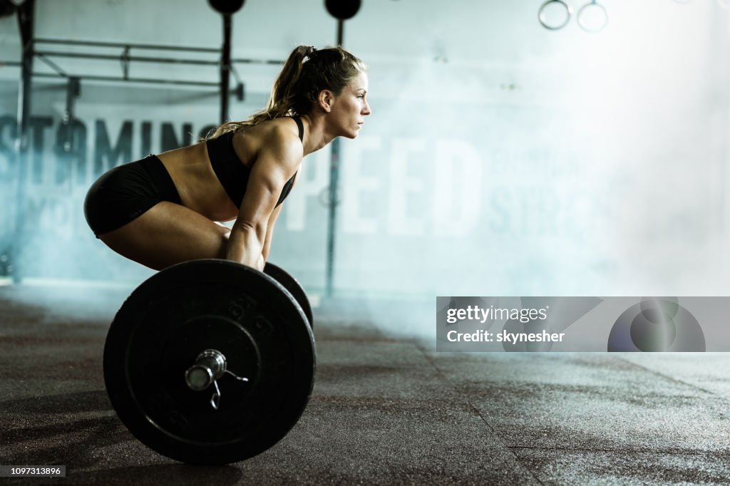 Vista lateral de mujer atlética ejercicio de peso muerto en un gimnasio.