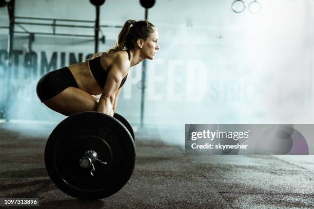 vista lateral de mujer atlética ejercicio de peso muerto en un gimnasio. - crossfit fotografías e imágenes de stock