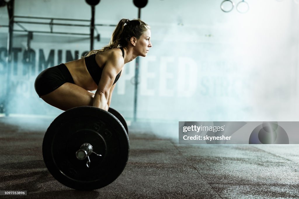 Side view of athletic woman exercising deadlift in a gym.