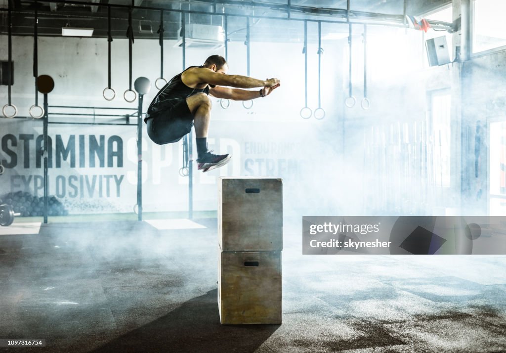 Seitenansicht des männlichen Athleten springen auf Kiste beim Sport-Training in einem Fitnessstudio.