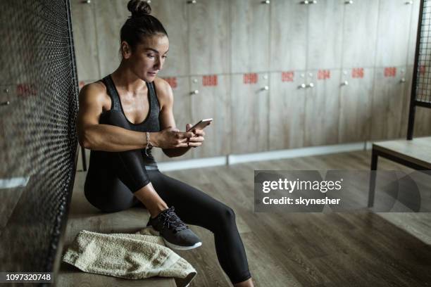 zweterige atletische vrouw met behulp van mobiele telefoon in de kleedkamer. - atlete stockfoto's en -beelden