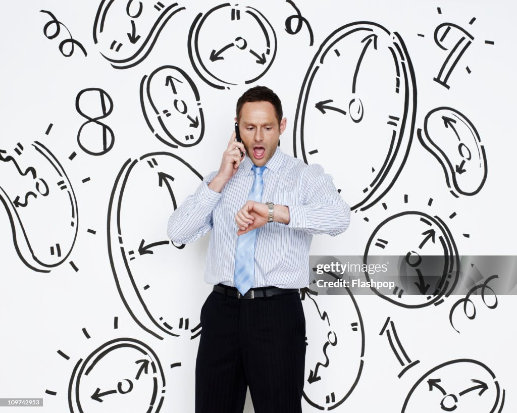Businessman looking at watch surrounded by clocks