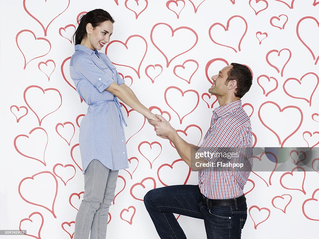 Man proposing to woman surrounded by love hearts