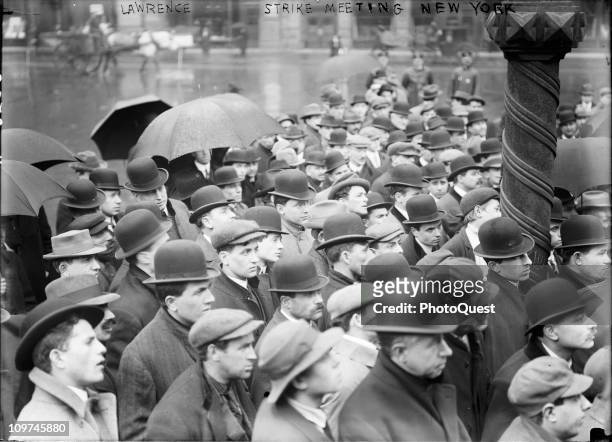 Group of men stand in the rain, while gathered outdoors to listen to the latest news about the Lawrence, Massachussetts textile strike, New York,...
