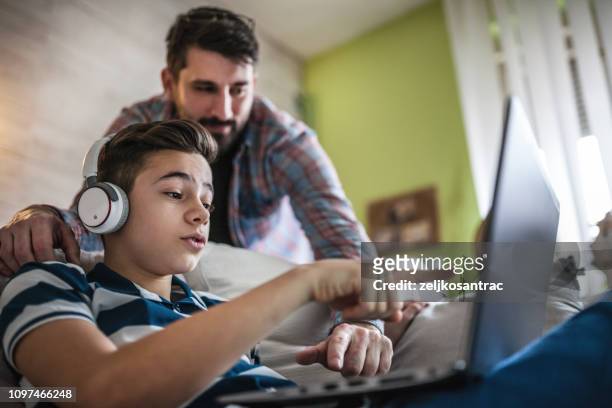 smiling father and son using digital gadgets in living room - parent on computer stock pictures, royalty-free photos & images