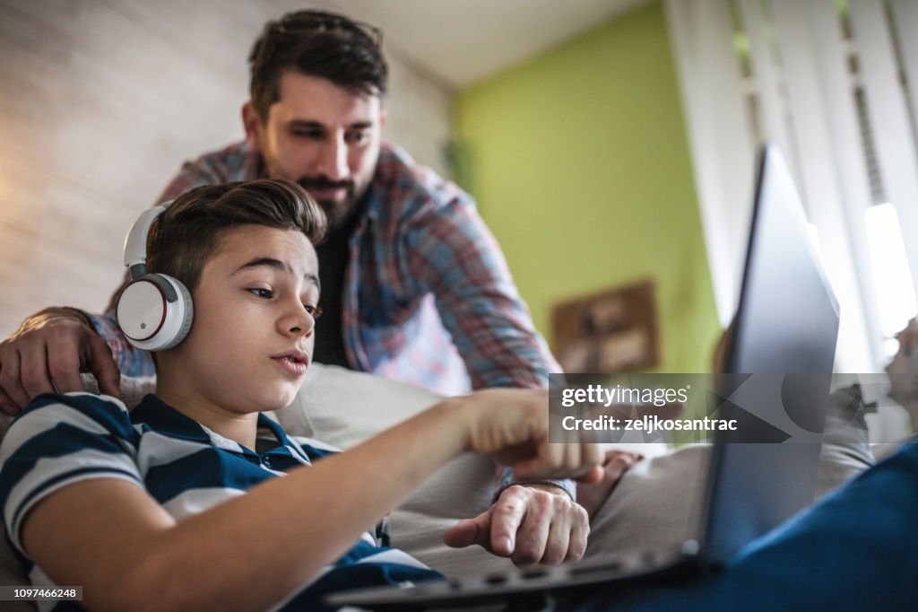 微笑的父親和兒子在客廳裡使用數位小玩意