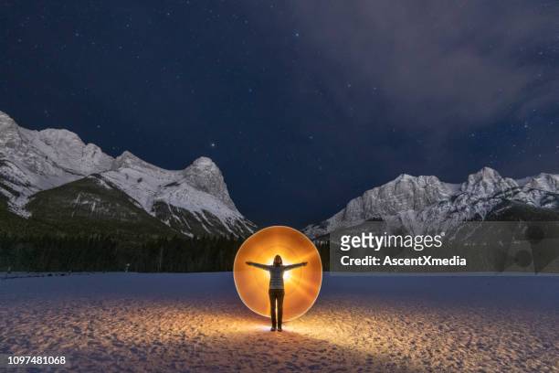 woman stands in snowy field below mountains with yellow light - freeze ideas stock pictures, royalty-free photos & images