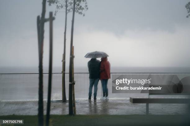 walking in the rain next to seaside - sharing umbrella stock pictures, royalty-free photos & images