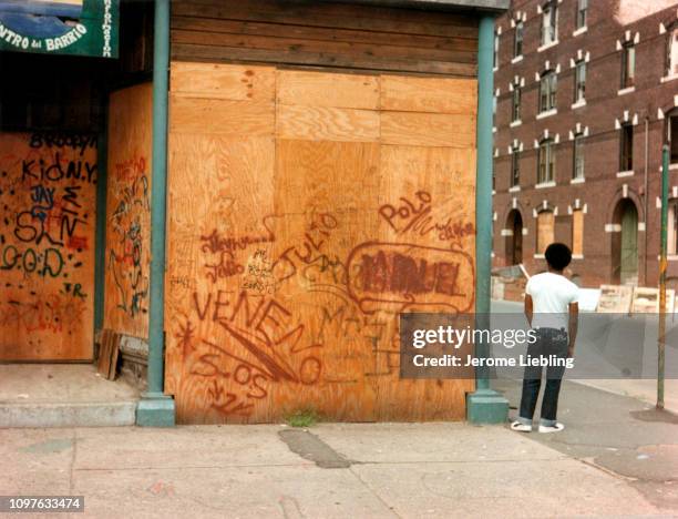 View from behind of an unidentified man with an afro pick in his pocket as he stands on the street beside a shuttered storefront covered with...