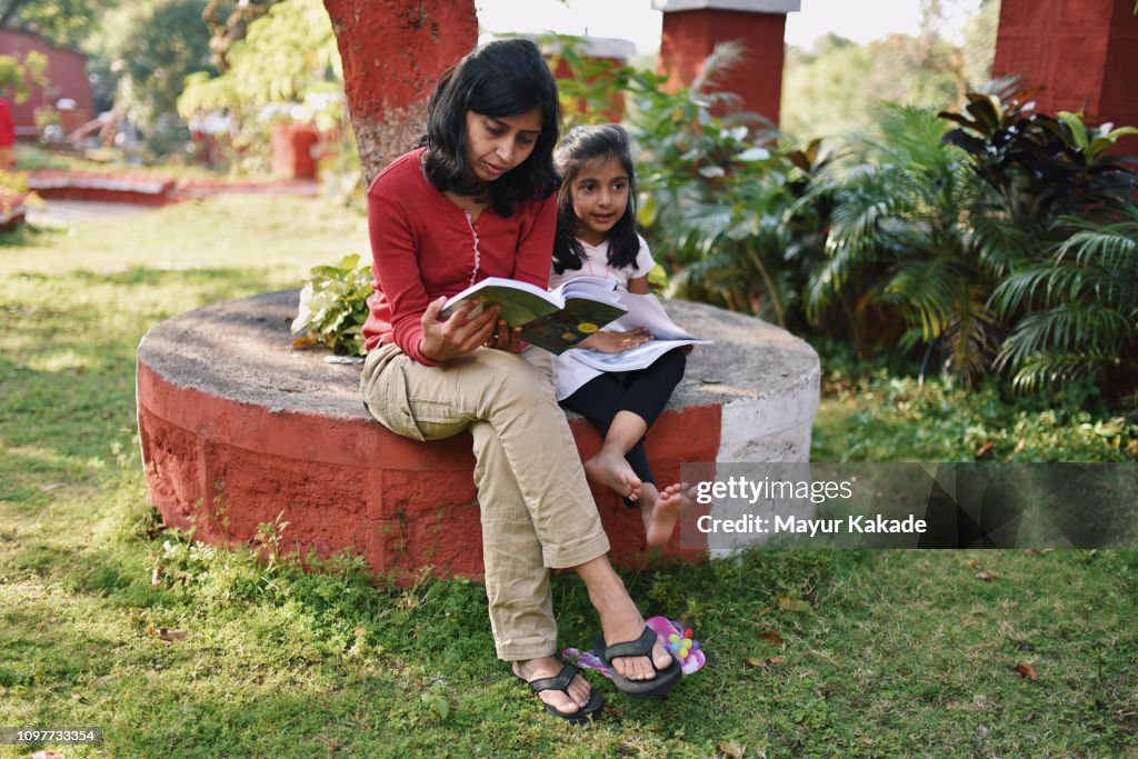 Young girl with mother reading book under the tree