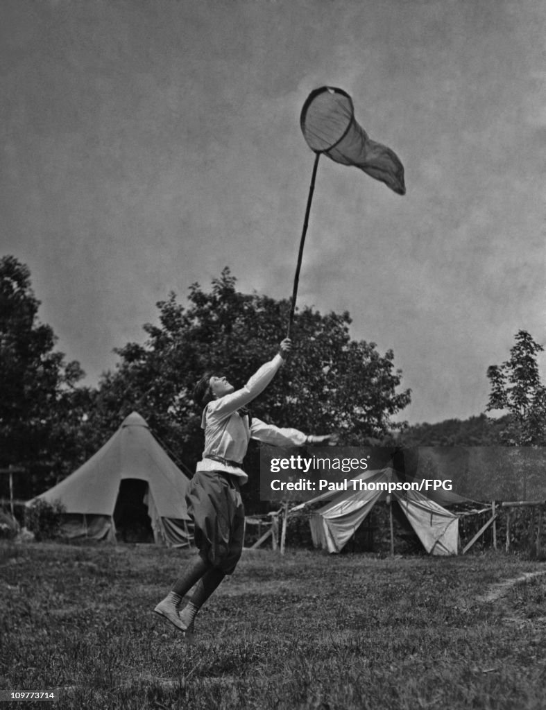 A Girl Guides trying to catch something in a net at a camp circa 1920 ...