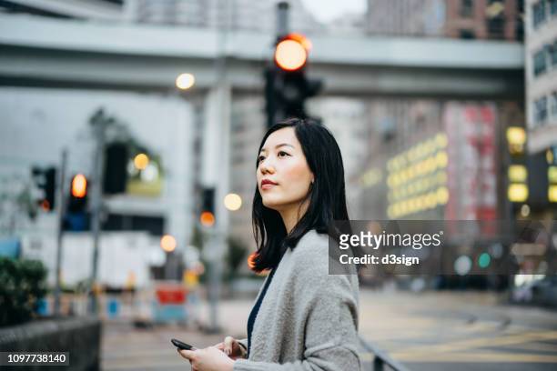 young woman with smartphone commuting in the city, against busy city traffic and highrise buildings - hong kong mass transit fotografías e imágenes de stock
