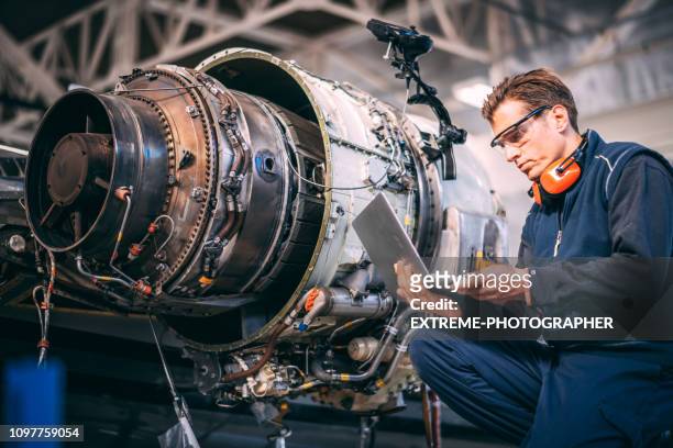 vliegtuig ingenieur in een loods met behulp van een laptop tijdens het repareren en onderhouden van een straalmotor vliegtuig - part of stockfoto's en -beelden