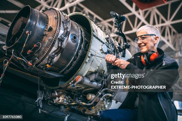 ingeniero de avión mujer mayor con un destornillador desatornillar una parte de un pequeño motor de jet en un avión privado durante el mantenimiento en un hangar para aviones - airplane part fotografías e imágenes de stock