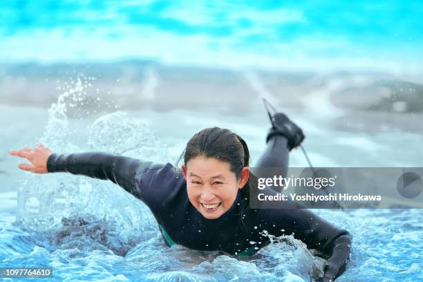 surfer paddling with surfboard on japanese beach in splash. - active seniors surfing stock pictures, royalty-free photos & images