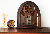 Close up view of antique wooden radio and broken clock with white wall in background