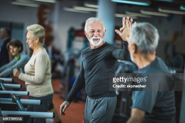 gelukkig senior mannen geven elkaar hoge vijf op loopbanden in een sportschool. - active senior man stockfoto's en -beelden