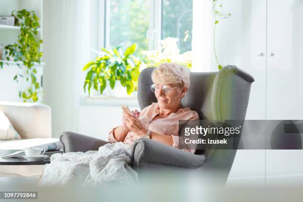 elderly lady using a smart phone in her room - senior comfortable stock pictures, royalty-free photos & images