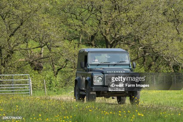 Farmer driving a Land Rover Defender over a field, Lancashire, UK.