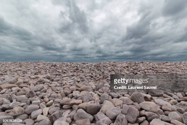 between sky and stones, full frame image containing a gray cloudy moody sky and a beach of pebbles - laurent sauvel photos et images de collection
