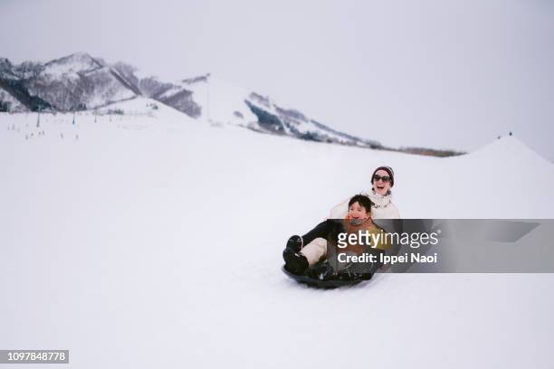 mother and child having fun with tobogganing on snowy mountain - family snow stock pictures, royalty-free photos & images