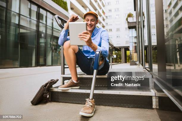 homem com perna protética, sentado na frente do prédio enquanto falava sobre um tablet digital - leg - fotografias e filmes do acervo