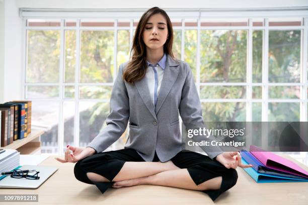 businesswoman doing yoga exercise on desk in a loft - lotuspositie stockfoto's en -beelden