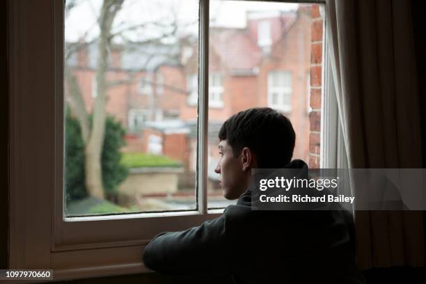 teenage boy looking out of bedroom window - boy sad foto e immagini stock