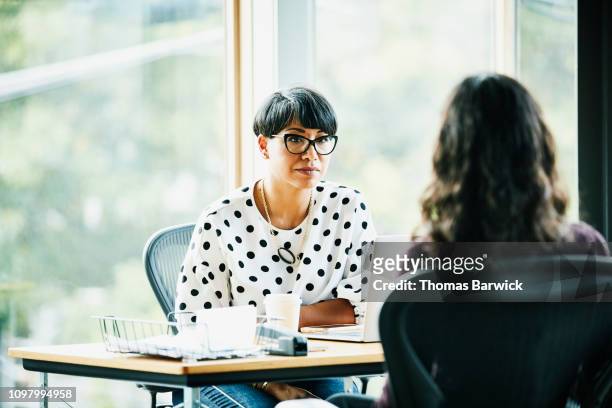 mature businesswoman in discussion with employee while seated at workstation in office - due persone foto e immagini stock