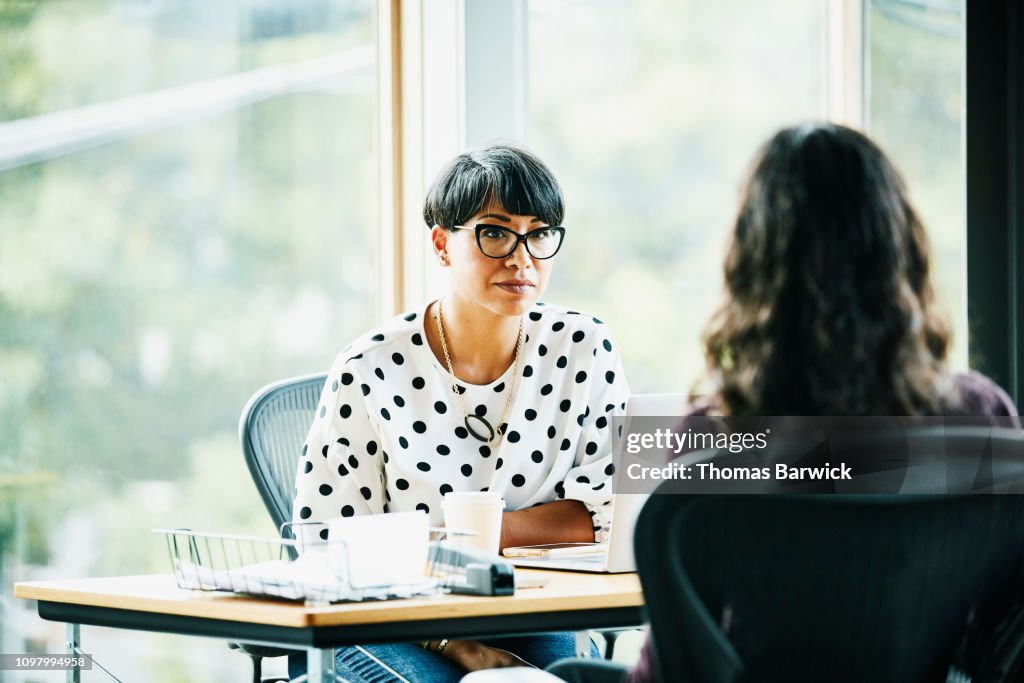 Mature businesswoman in discussion with employee while seated at workstation in office