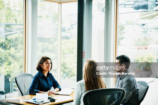 smiling businesswoman in discussion with clients at office workstation - cliente fotografías e imágenes de stock
