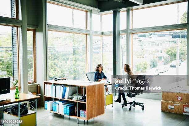 businesswomen discussing project while seated at office workstation - agence-de-design photos et images de collection