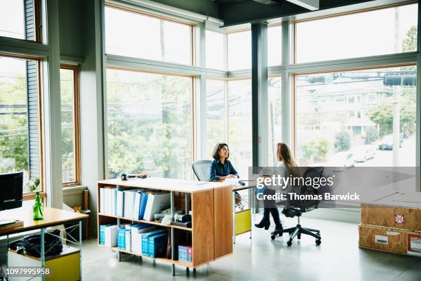 businesswomen discussing project while seated at office workstation - design studio stock pictures, royalty-free photos & images