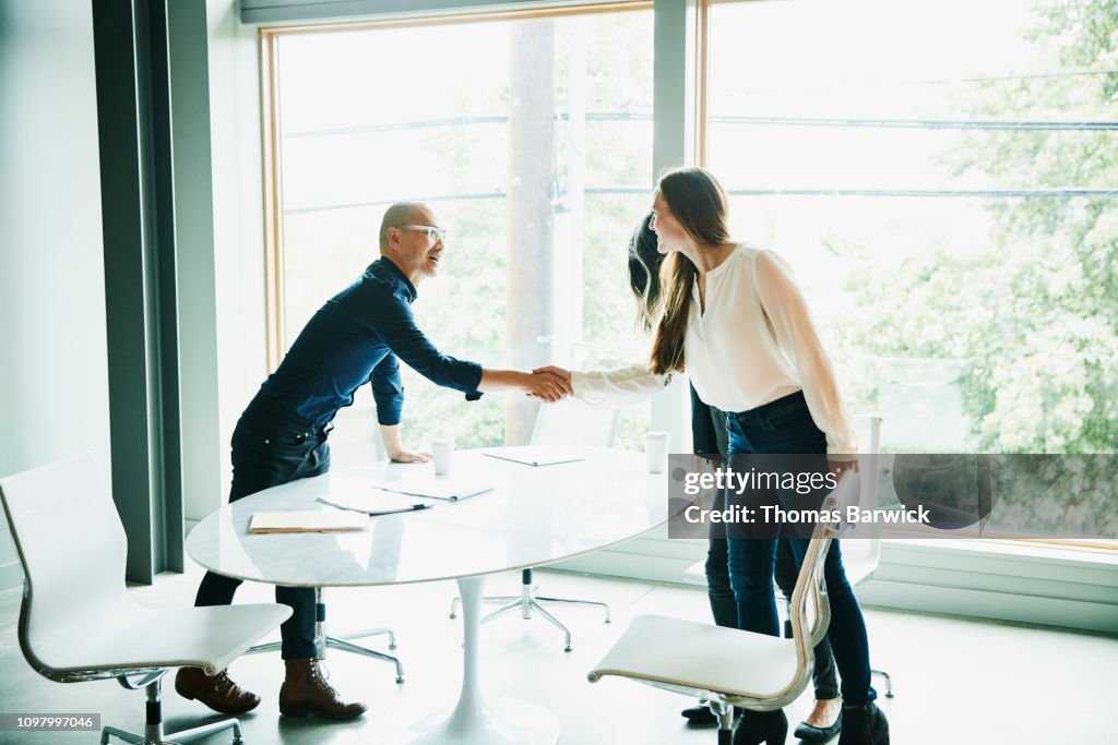Businesswoman shaking hands with client before meeting in office conference room