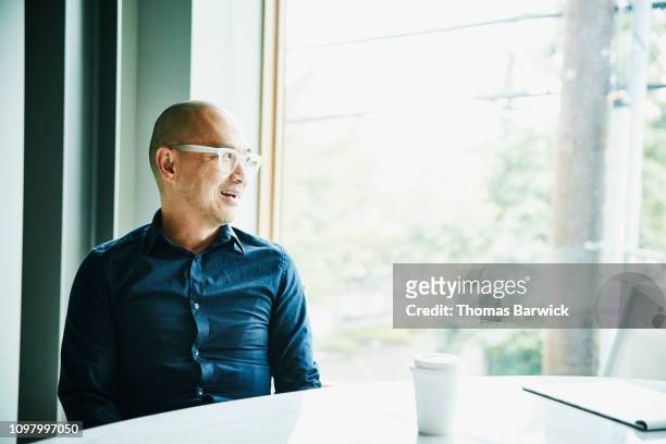 portrait of mature businessman sitting in office conference room looking out window - front view bildbanksfoton och bilder