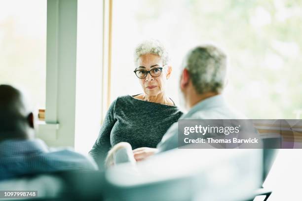 senior businesswoman listening to presentation from coworker during meeting in office - lady grey background stock pictures, royalty-free photos & images