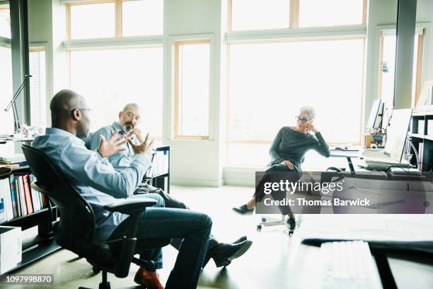 business colleagues in discussion while seated at workstations in design studio - design studio stock pictures, royalty-free photos & images